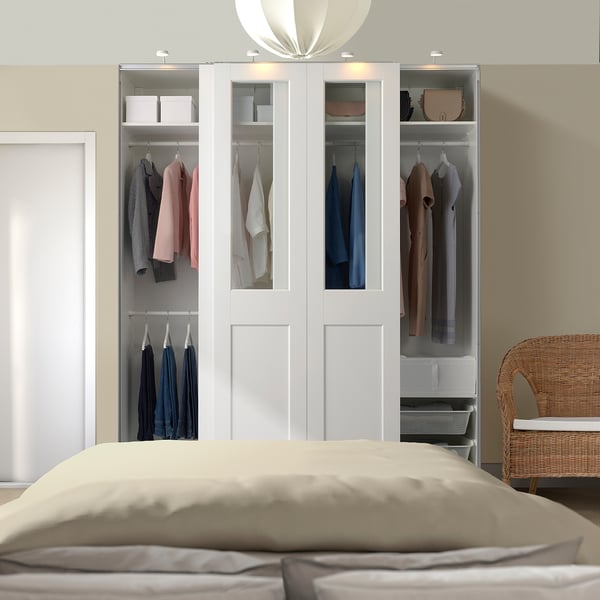 White PAX wardrobe with glass doors, tall and spacious beside bed and wicker chair.