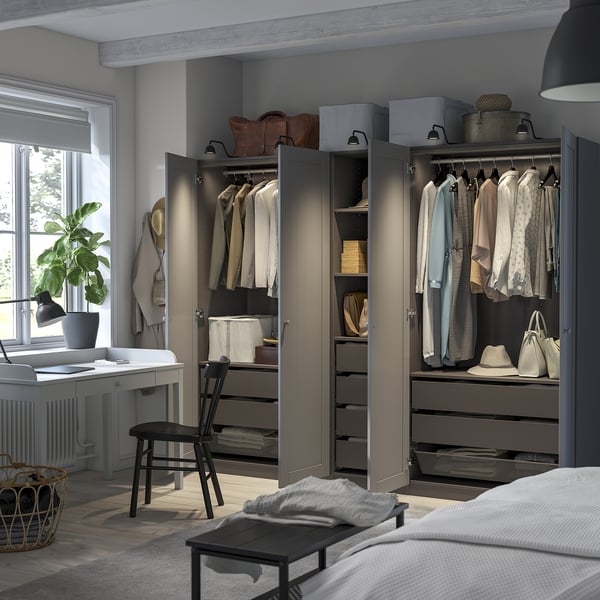 Modern bedroom with open wardrobe showcasing clothes, drawers, and accessories; includes desk with chair and plant.