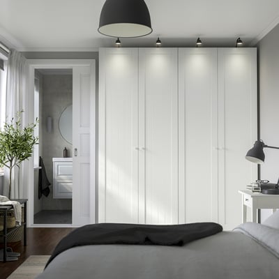 Minimalist bedroom with white wardrobes, grey bed, large black lamp, and small plant.