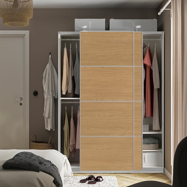 Wooden sliding closet, open showing clothes hangers, shelves with folded garments, above are storage boxes in bedroom.