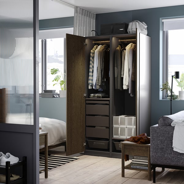 A modern bedroom an open PAX wardrobe filled with clothes. It has drawers, a hanging rail, and baskets.
