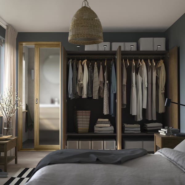 Bedroom with open wardrobe displaying clothes, folded clothes, and storage bins. Closet has wooden finish and adjustable interiors.