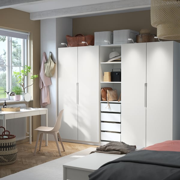 A bedroom with a large white PAX wardrobe, multiple shelves, and drawers. The wardrobe is central, modern, with a red bedspread and wooden flooring.