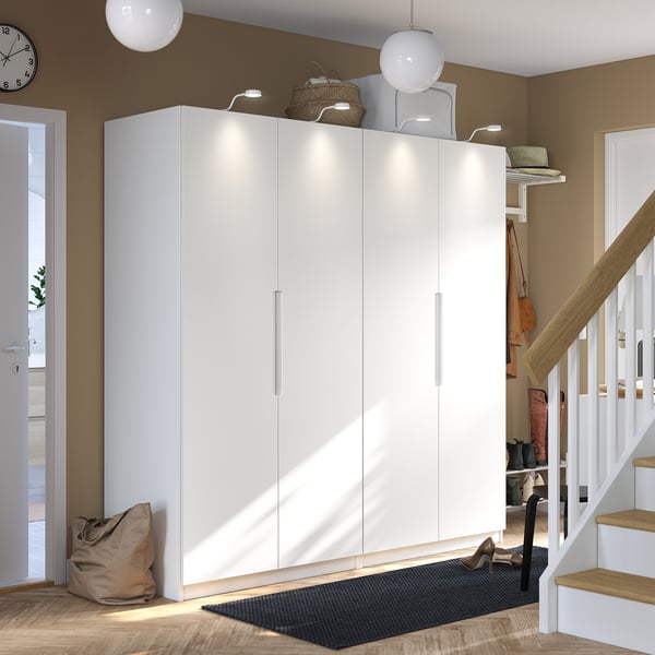 Large white PAX wardrobe with minimalist design stands tall, reaching ceiling height. Surrounded by small items, its large and prominent.