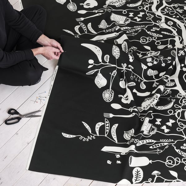 Person preparing black fabric with white playful food pattern for sewing project. Scissors and pins nearby.