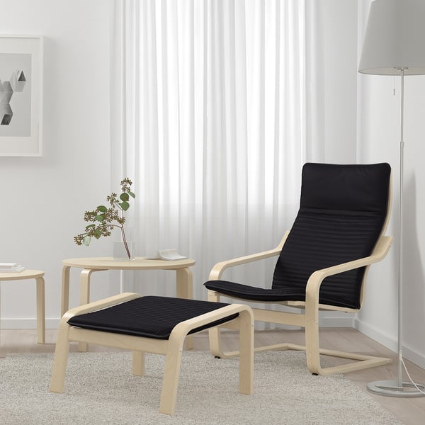 Minimalist living room with POÄNG chair, footstool, light wood frame, rug, lamp, and vase.