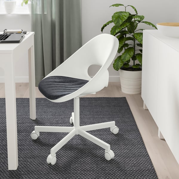 Modern office setup with a white desk, grey rug. Small, white, ergonomic chair with a blue cushion, between a plant and a laptop on desk.