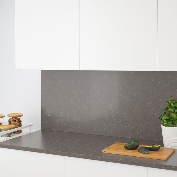 Modern kitchen with grey quartz countertop and backsplash. Avocados and cutting board on counter, jars to left, plant to right.