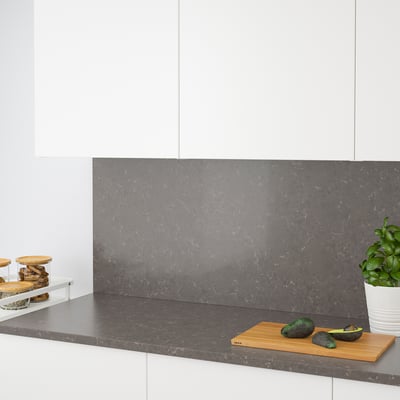 Modern kitchen with grey quartz countertop and backsplash. Avocados and cutting board on counter, jars to left, plant to right.