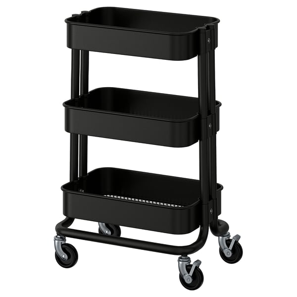 A black, three-tiered utility cart, RÅSKOG, with metal frames and plastic bins for storage and mobility.