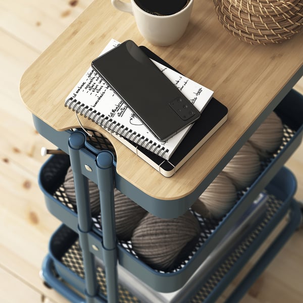 A RÅSKOG trolley storing yarn, notes, and a phone, demonstrating its use for various items and stability with lockable casters.