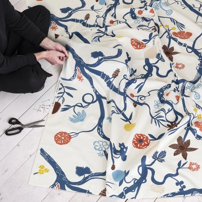 A person is cutting colourful floral-patterned fabric with scissors, preparing it for sewing.