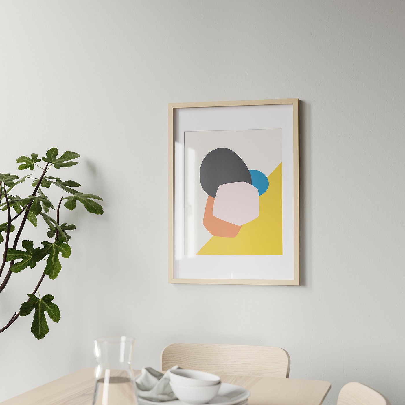 A modern wooden picture frame hangs on a wall, displaying colourful abstract art. Below it, a dining table holds glasses, cups, and a plant.