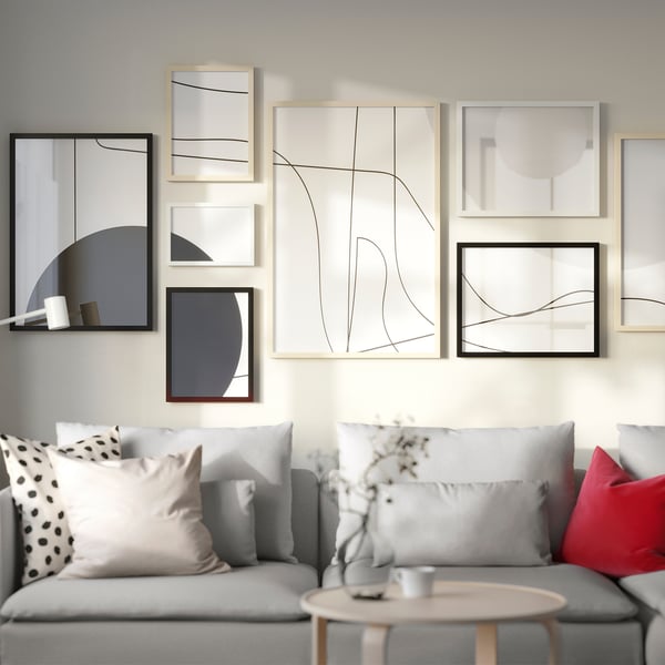 Modern living room with light grey sofa, colourful pillows, and abstract wall art in wooden frames.