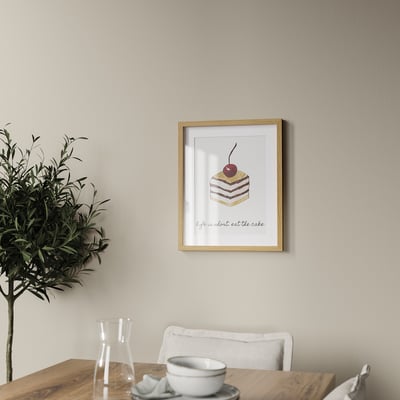 A framed cake photo on a wall above a table with plant, pitcher, and teacup.