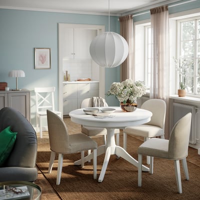 Cosy dining area with extendable table, beige chairs, blue walls, and white flowers.