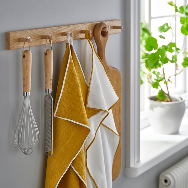 Kitchen utensils hang on wooden rack; whisk, grater, towels, cutting board.