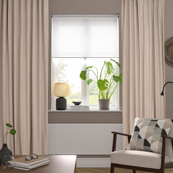 Modern living room with beige velvet curtains, chair, plant, and lamp, creating a cosy atmosphere.