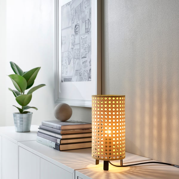 SAXHYTTAN table lamp on shelf, small, bamboo design, warm light, beside books & plant.