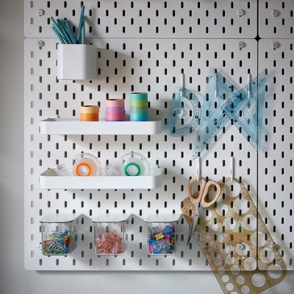 SKÅDIS pegboard storage: white, metallic grid holding containers, coloured tapes, tools, scissors, and rulers, ideal for desk organisation.