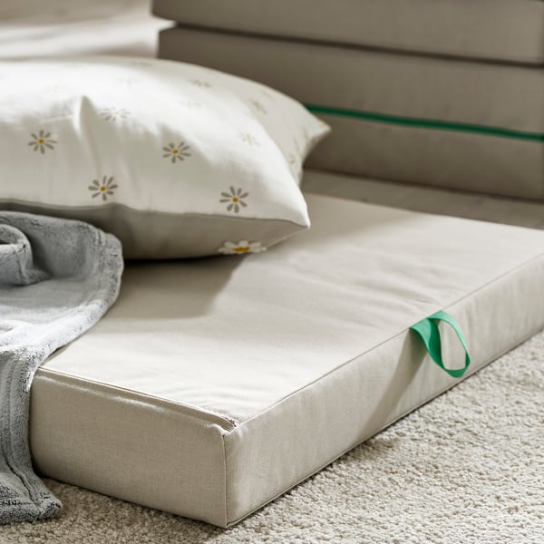 Modern bed with soft, folded mattress on floor, featuring flowered pillow and grey blanket, showcasing quality and comfort.
