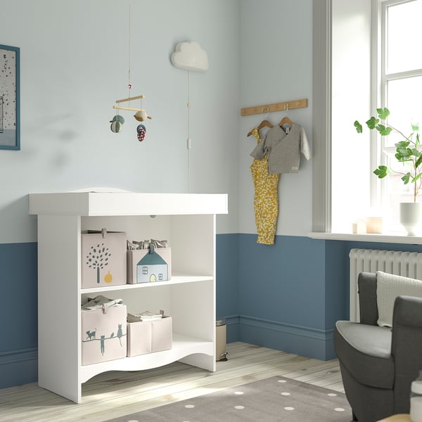 Nursery with blue walls, changing table, baby clothes, armchair, and plant.
