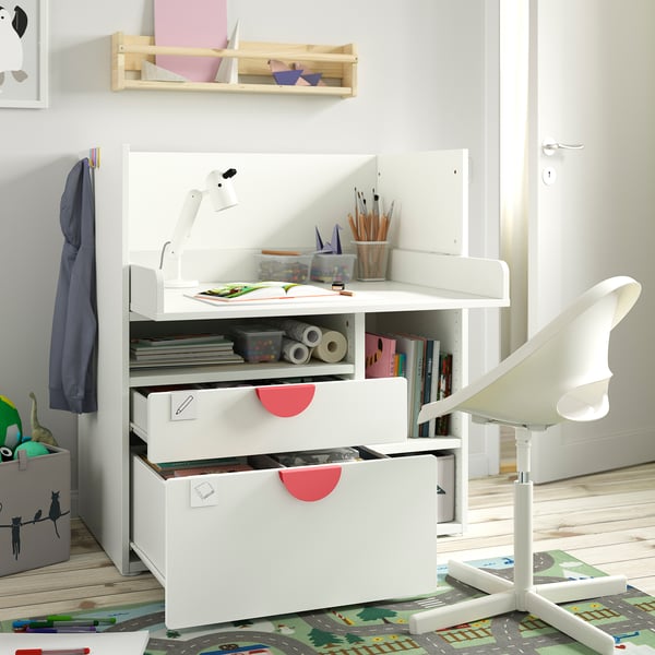 A white kids desk with drawers and shelves, storing art supplies. A chair and lamp are attached, promoting learning and creativity.