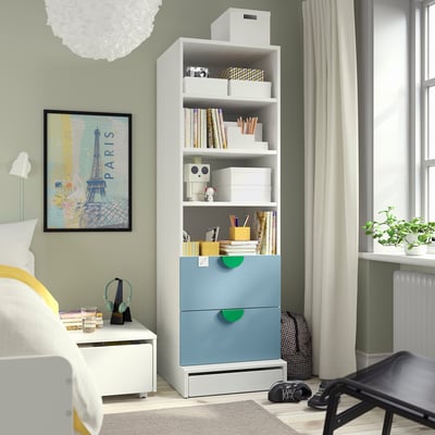 Modern bedroom with blue SMÅSTAD bookcase, bed, paris poster, and plants.