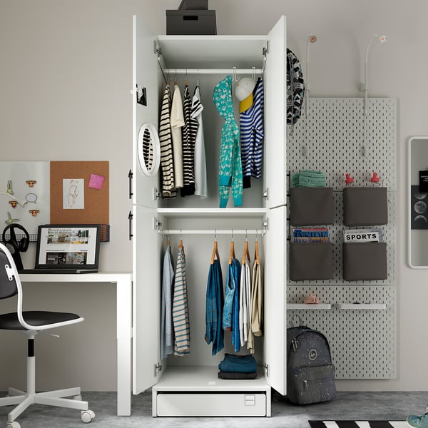 An open white SMÅSTAD wardrobe, storing colourful clothes and bags, beside a furniture with a laptop, chair, and organised accessories.