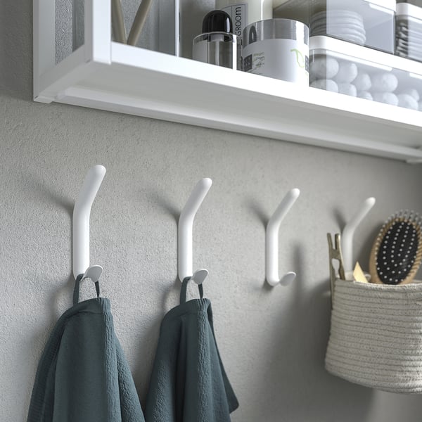 White double hooks on wall with towels hanging, shelf above with bathroom items.