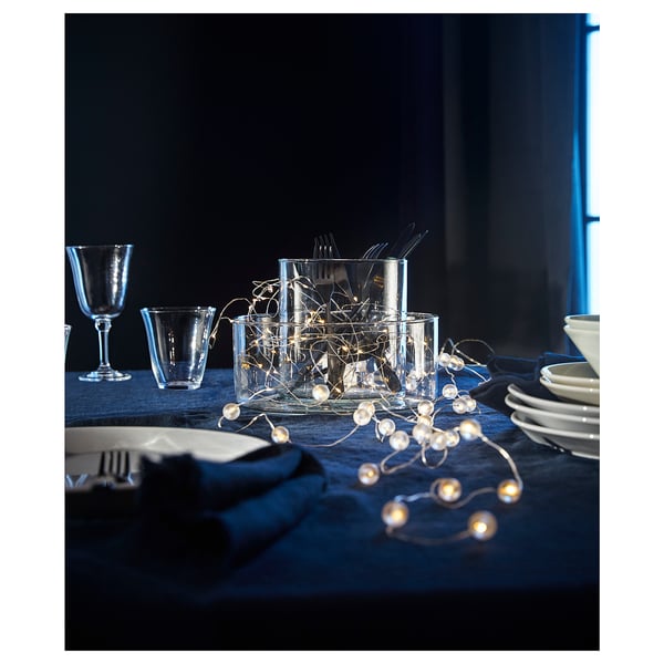 Table set with blue cloth, glassware, cutlery, and SNÖYRA string lights. Decorative, festive ambiance.