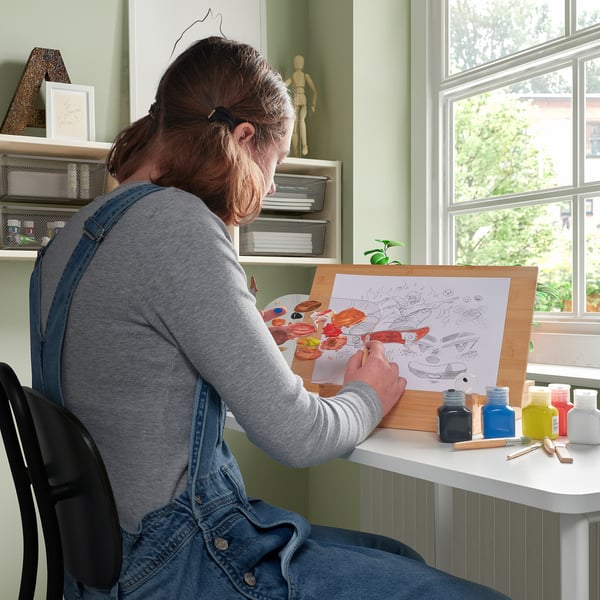 Person painting with SOLFÅGEL acrylics at a desk, vibrant colours nearby.