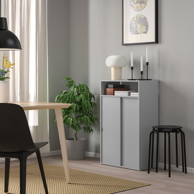 Modern SPIKSMED cabinet in grey with sliding doors, open/closed storage, minimalist design between plant and stool.
