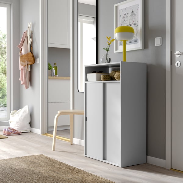 Modern entryway with grey SPIKSMED cabinet, sliding doors, yellow lamp, coat hooks, and wooden stool, fitting neatly beside grey door.