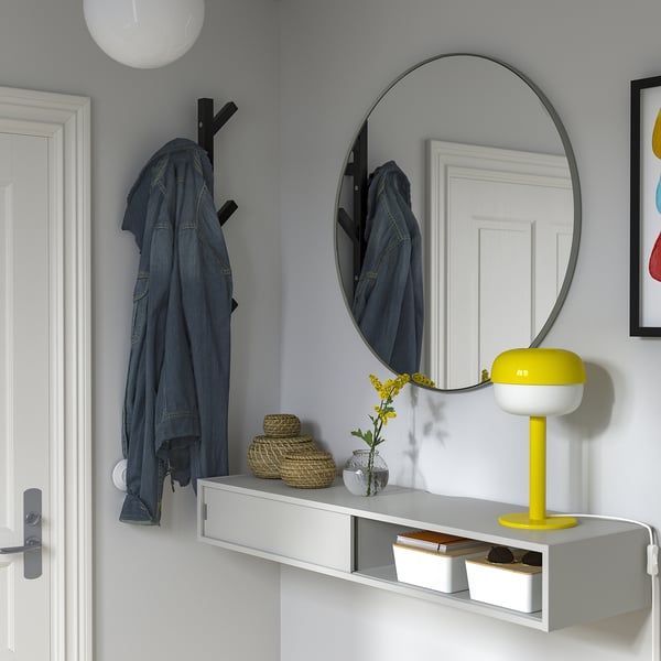 Modern entryway with grey wall, shelf has denim jacket, lamp, flowers, mirror, and storage.