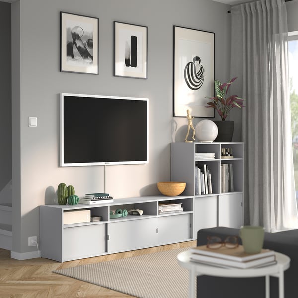 Modern living room with white tv bench, shelves, and decorations. Grey wall, abstract art, plant, bowls, books, rug, hardwood floor.