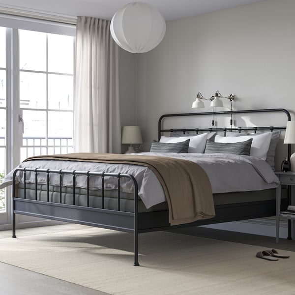 Modern minimalist bedroom with large STJÄRNÖ bed, featuring a black metal frame, white linens, and large window with curtains.