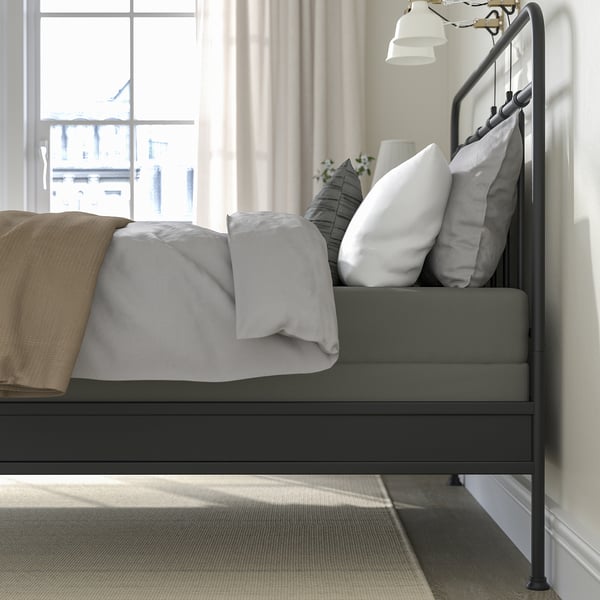 Modern minimalist bedframe with metal headboard near a large window, dressed in light grey and beige bedding.