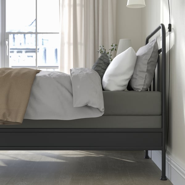 Modern bed frame with metal headboard, lyngör base, & mattress cover. Light grey, cosy pillows, tan blanket, large window.