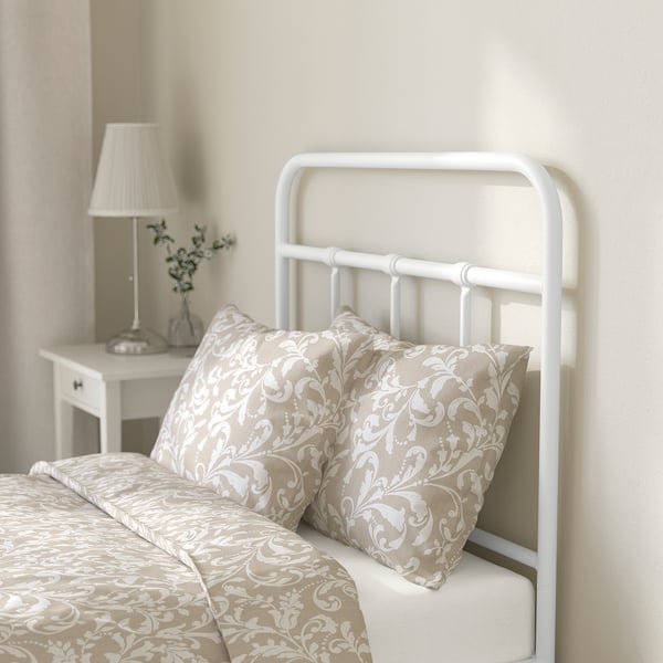 Bed with curved headboard, pillows, bedside table lamp, beige patterned decor.
