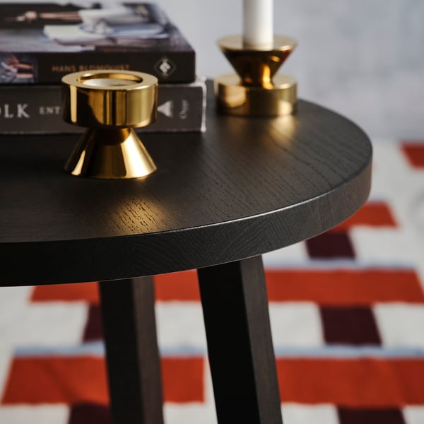 Black round side table with gold candle holders, on a red patterned rug.