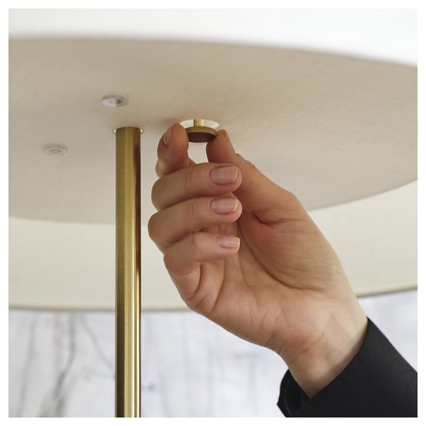 Person assembling modern lamp with brass foot and travertine base.