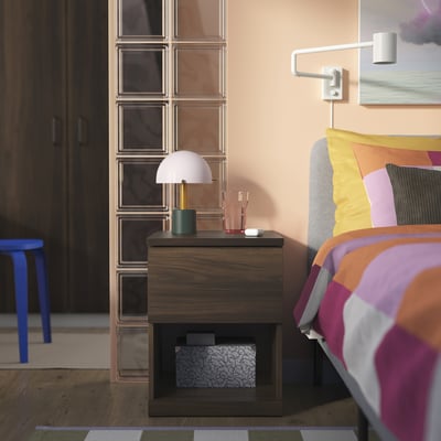 Bedroom with STORKLINTA wooden bedside table, white lamp, colourful bedding, and wall light.