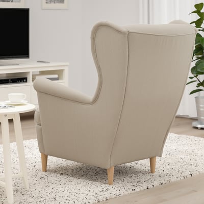 Beige wingback chair in living room with teacup set and tv.