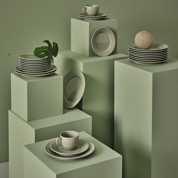 STRIMMIG series in sage on green pedestals - plates, cups, and bowls balanced in stacks, highlighting organic textures and modern details.
