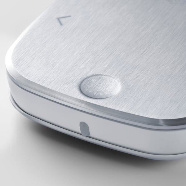 A sleek, stainless-steel remote control with a brushed finish, featuring a sun icon button.