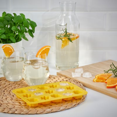 Two glasses with orange slice garnish beside a yellow ice cube tray and a pitcher of water with orange slices and rosemary.