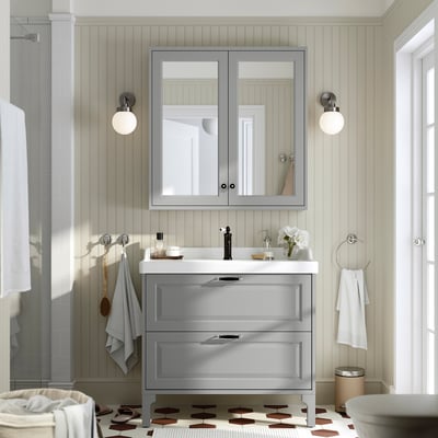 Modern grey bathroom with TÄNNFORSEN sink cabinet, mirrored medicine cabinet, chrome fixtures, and geometric-patterned floor mat.
