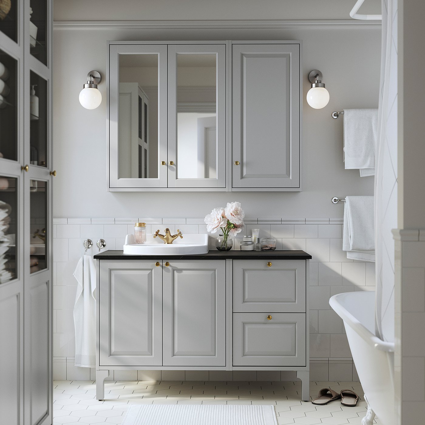 Modern bathroom with grey vanity, gold accents, mirrored cabinets, white sink, and claw-foot tub.