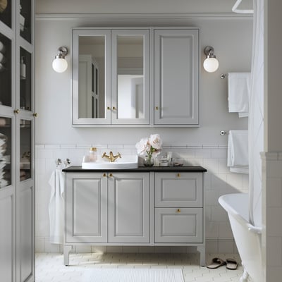 Modern bathroom with grey vanity, gold accents, mirrored cabinets, white sink, and claw-foot tub.